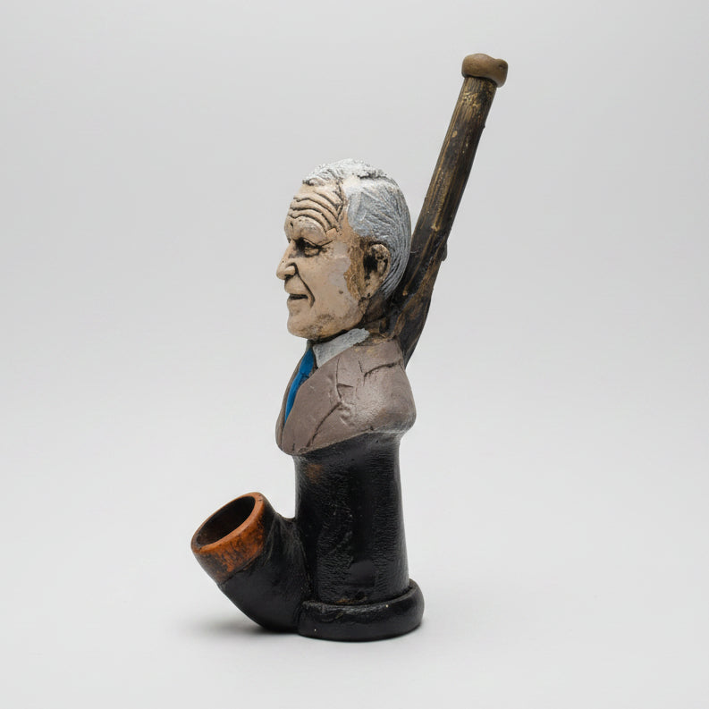 A ceramic figurine of a man's bust holding a baseball bat, displayed on a white table in front of a window.