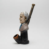 A ceramic figurine of a man's bust holding a baseball bat, displayed on a white table in front of a window.