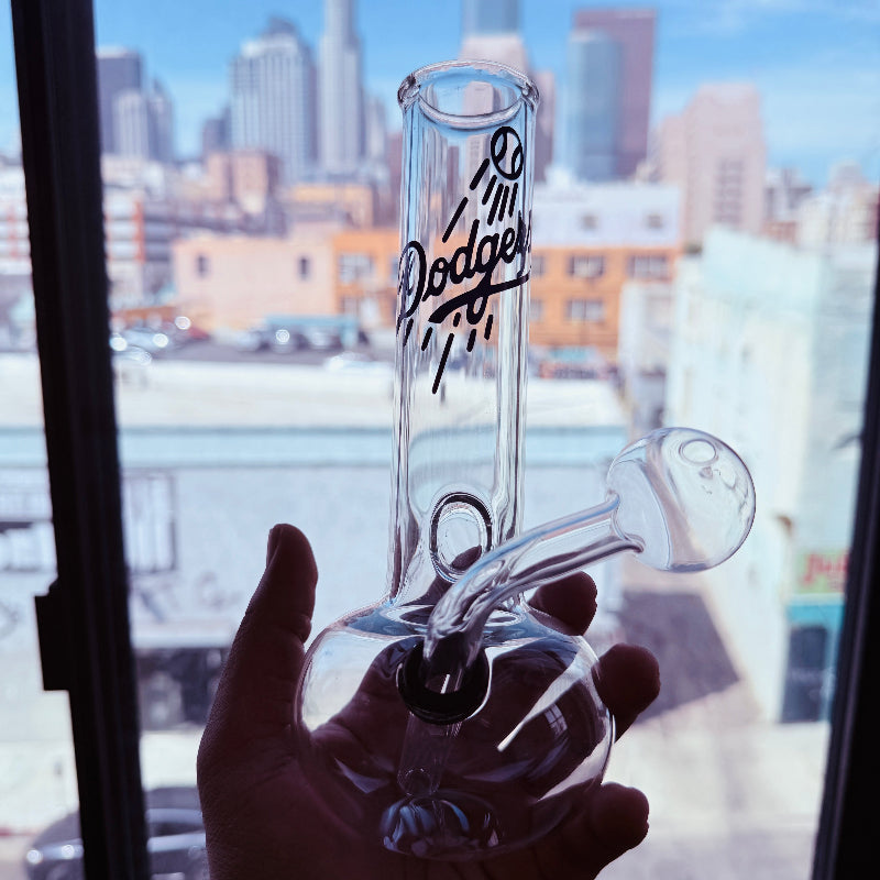 Glass bong with 'Dodgers' branding held in front of a cityscape.
