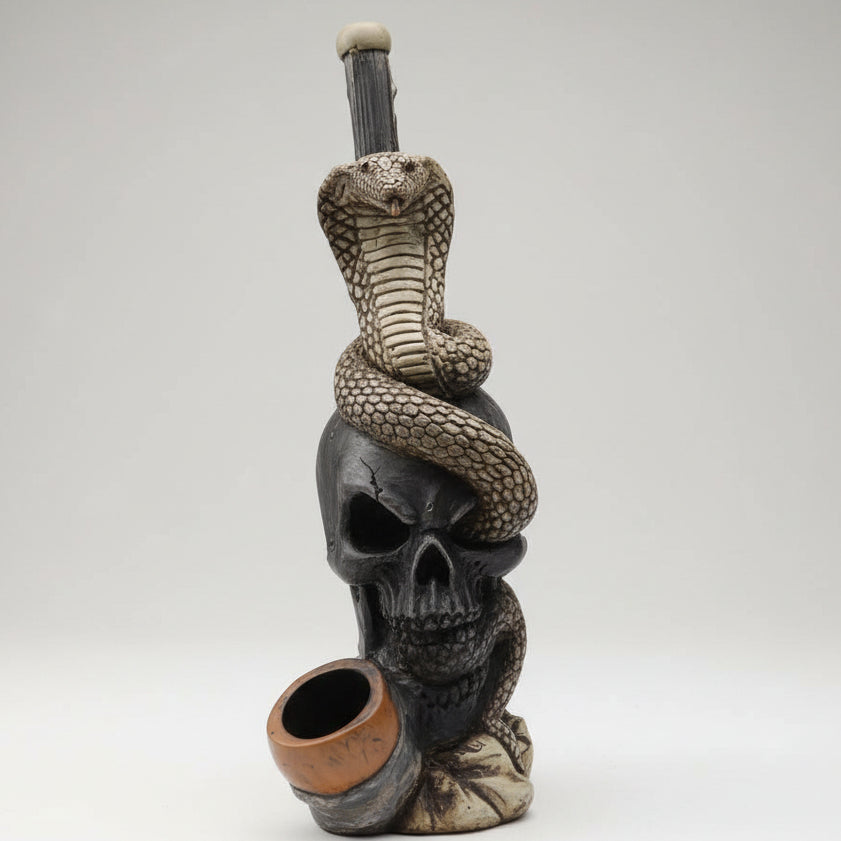 A decorative skull sculpture with a coiled snake draped over it and a small bowl or cup in front, displayed on a white tabletop near a large window with an outdoor city view.