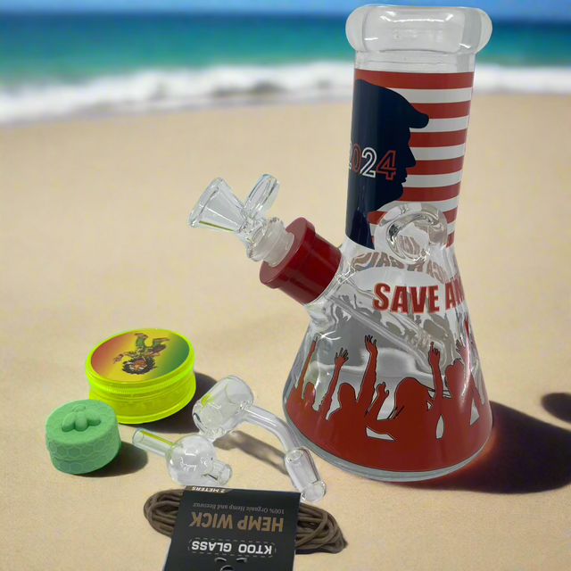 Trump 2024 Bong Box with premium design featuring bong, grinder, silicone container, quartz banger, hemp wick, carb cap, downstem, and dabber set on beach.